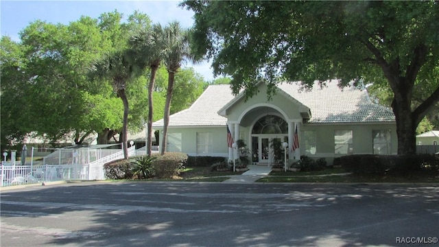 view of front of property featuring a tiled roof, fence, french doors, and stucco siding