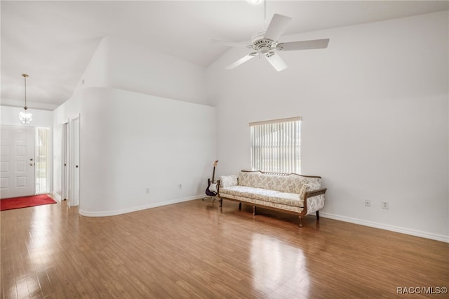 sitting room with ceiling fan with notable chandelier, wood finished floors, baseboards, and high vaulted ceiling