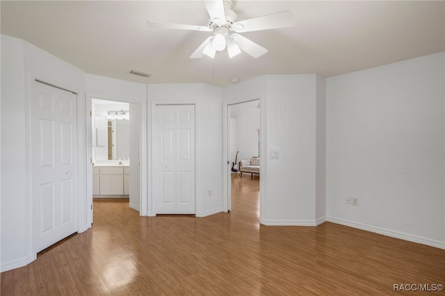 unfurnished bedroom with visible vents, ensuite bath, wood finished floors, baseboards, and ceiling fan