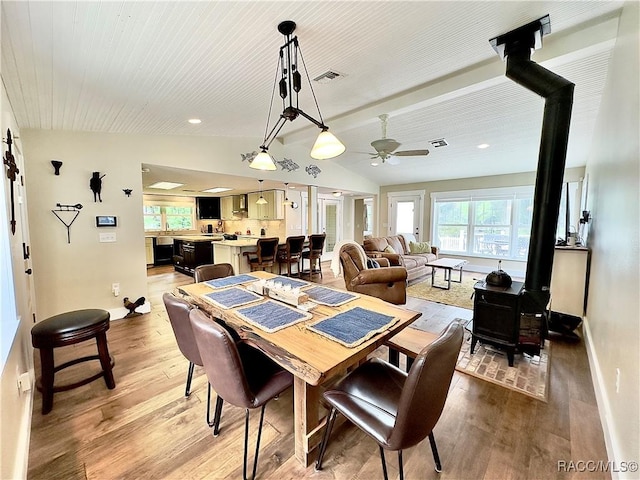 dining area featuring light wood-type flooring, vaulted ceiling, a healthy amount of sunlight, and a wood stove