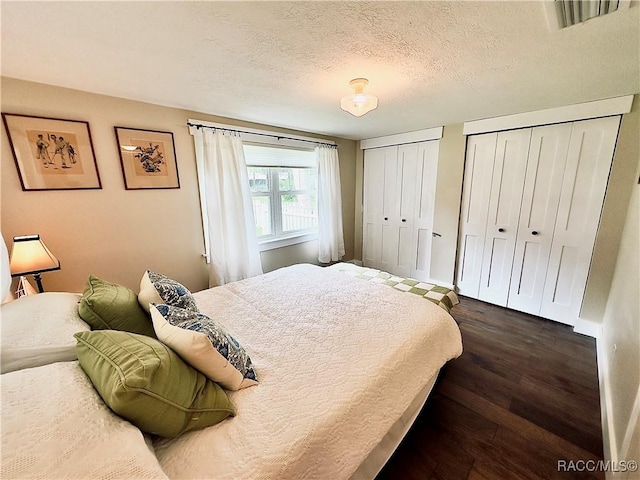 bedroom featuring dark hardwood / wood-style flooring, a textured ceiling, and two closets