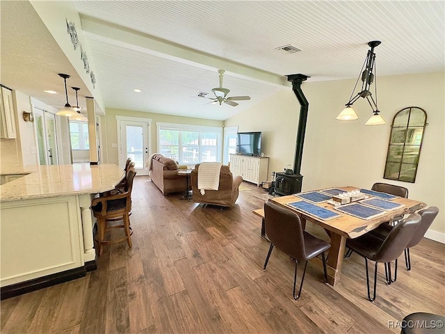 dining space with hardwood / wood-style floors, vaulted ceiling, ceiling fan, and a wood stove