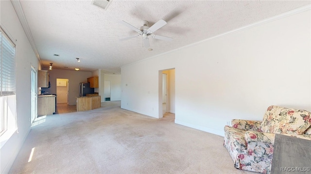 unfurnished living room with crown molding, a textured ceiling, ceiling fan, light colored carpet, and visible vents