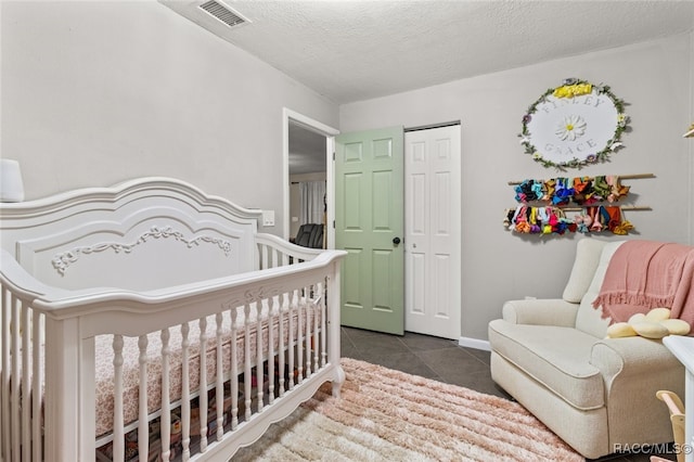 bedroom featuring a closet, dark tile patterned floors, a nursery area, and a textured ceiling