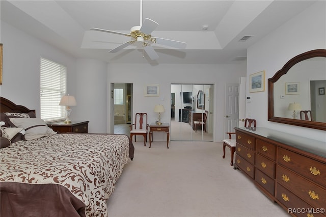 bedroom featuring a tray ceiling, ceiling fan, a closet, and light colored carpet