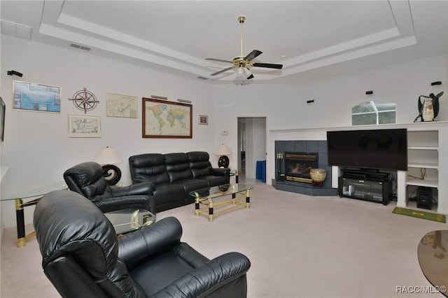 living room with carpet flooring, a raised ceiling, and a tiled fireplace