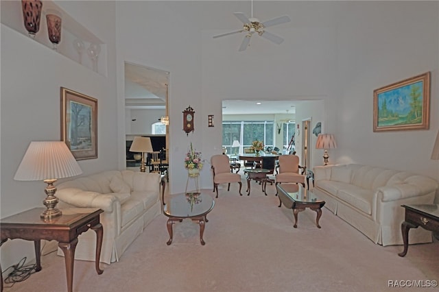 living room with ceiling fan, light colored carpet, and a high ceiling