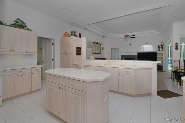 kitchen featuring ceiling fan, a center island, sink, a raised ceiling, and light tile patterned floors