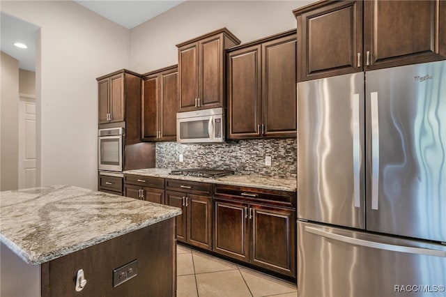 kitchen with stainless steel appliances, a kitchen island, dark brown cabinetry, light tile patterned flooring, and tasteful backsplash