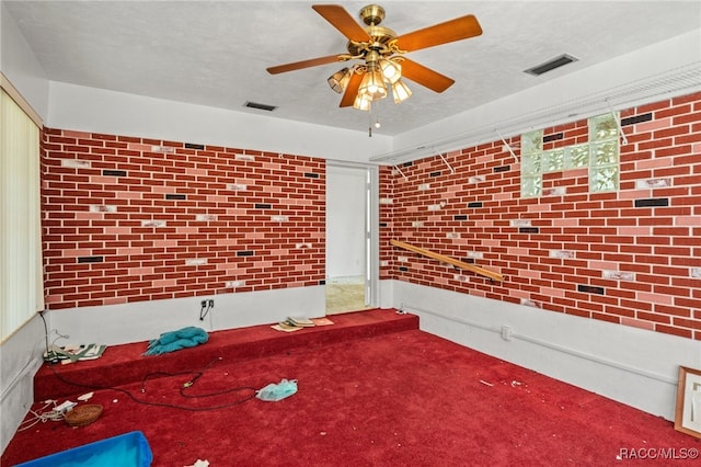 interior space with a textured ceiling, ceiling fan, and brick wall