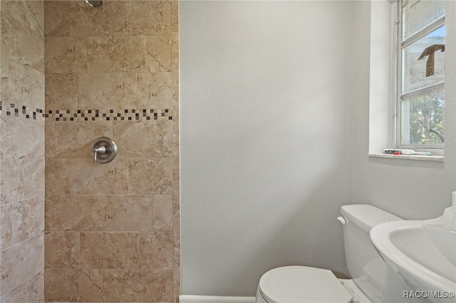 bathroom with a tile shower, toilet, and a wealth of natural light