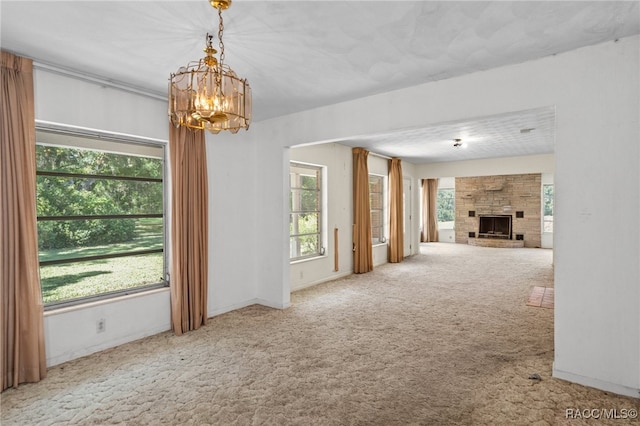 unfurnished living room featuring a healthy amount of sunlight, carpet floors, a fireplace, and an inviting chandelier