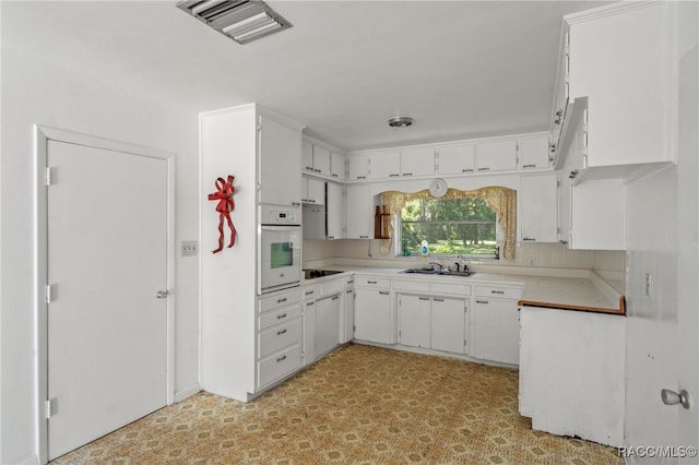 kitchen with black electric stovetop, oven, white cabinetry, and sink