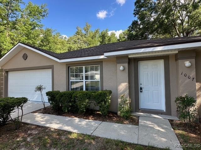 view of exterior entry with stucco siding, a garage, and driveway