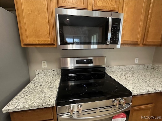 kitchen featuring stainless steel appliances, brown cabinetry, and light stone countertops