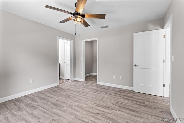 unfurnished bedroom featuring baseboards, visible vents, ceiling fan, a walk in closet, and light wood-type flooring