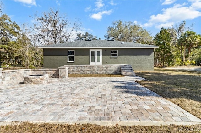 rear view of house with stucco siding, an outdoor fire pit, a patio area, and french doors