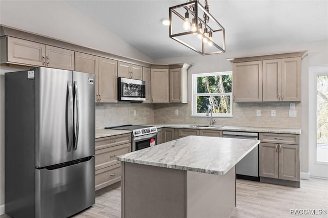 kitchen featuring a sink, vaulted ceiling, appliances with stainless steel finishes, a center island, and tasteful backsplash