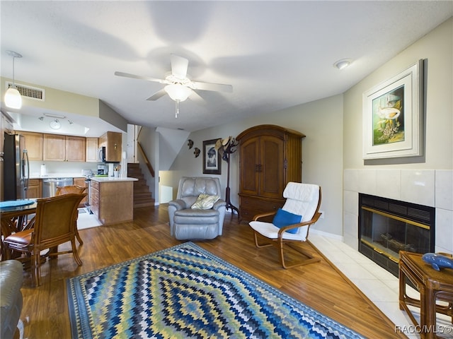 living room with hardwood / wood-style floors, ceiling fan, and a tile fireplace