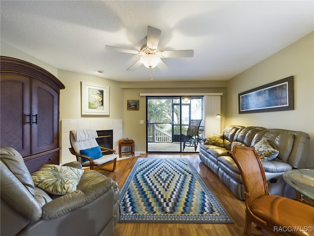 living room with hardwood / wood-style floors, ceiling fan, a textured ceiling, and a tiled fireplace