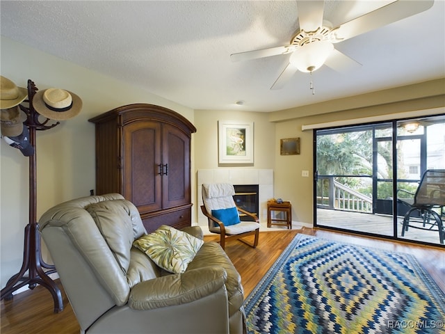 living room with hardwood / wood-style floors, a textured ceiling, ceiling fan, and a tiled fireplace