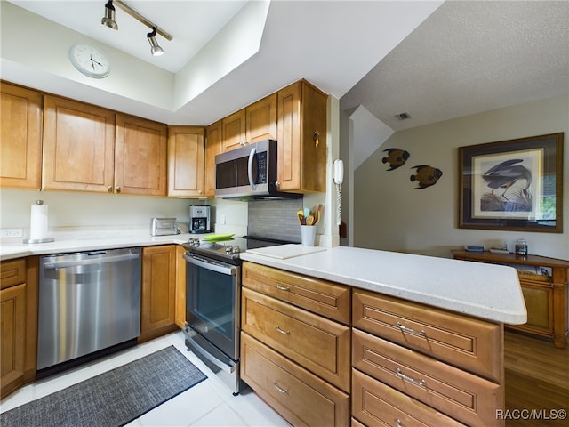 kitchen with kitchen peninsula, appliances with stainless steel finishes, track lighting, a textured ceiling, and light tile patterned floors