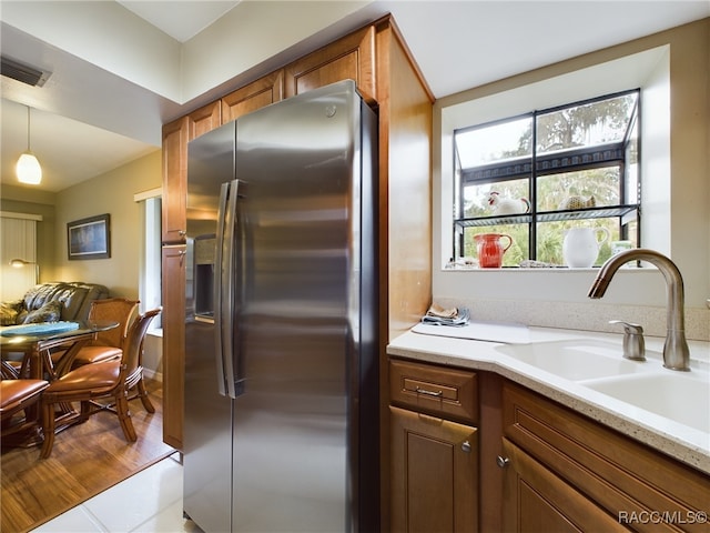 kitchen with light stone counters, sink, stainless steel fridge with ice dispenser, light hardwood / wood-style floors, and hanging light fixtures