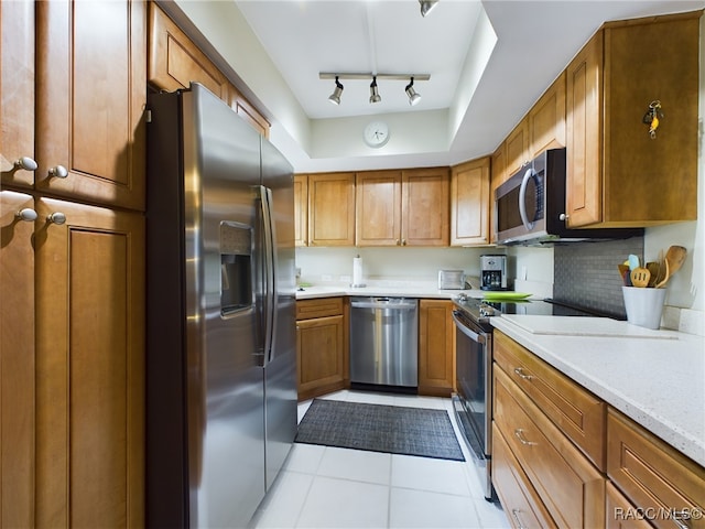 kitchen featuring light stone countertops, backsplash, track lighting, stainless steel appliances, and light tile patterned flooring