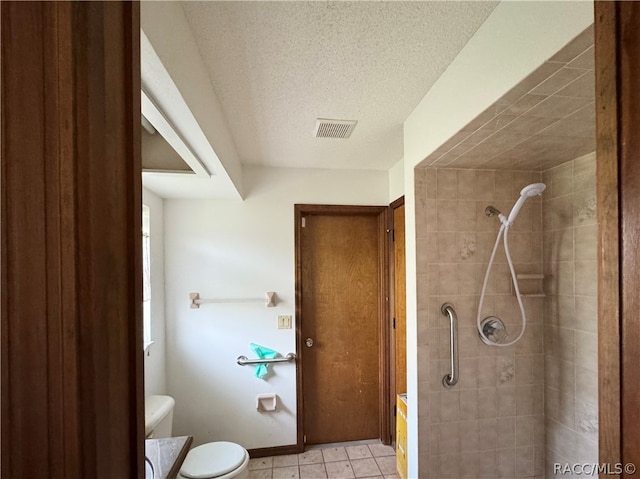 bathroom with a tile shower, tile patterned floors, a textured ceiling, toilet, and vanity