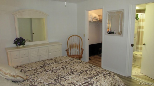 bedroom featuring ensuite bathroom, a walk in closet, wood finished floors, and a closet