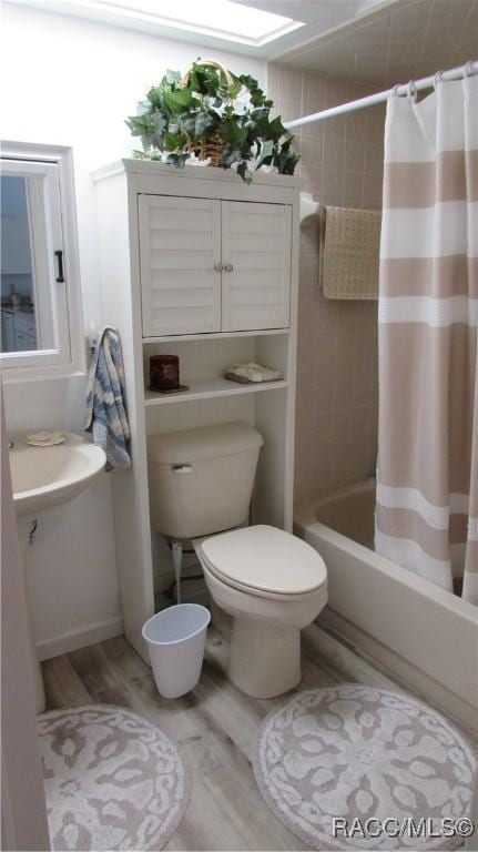 bathroom featuring toilet, shower / bathtub combination with curtain, and wood finished floors