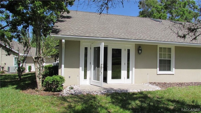 rear view of house with a lawn, stucco siding, cooling unit, and roof with shingles