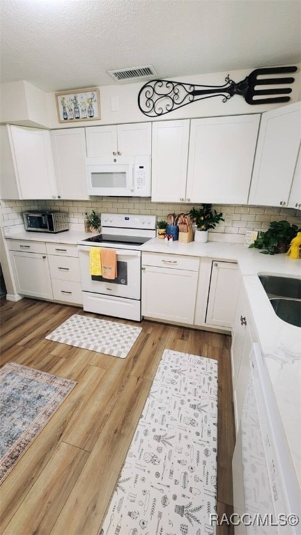 kitchen featuring decorative backsplash, light wood-type flooring, a textured ceiling, white appliances, and white cabinetry