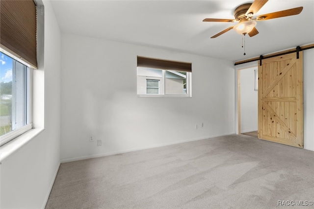 carpeted spare room with ceiling fan and a barn door