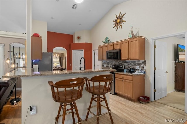 kitchen with light stone counters, a kitchen bar, appliances with stainless steel finishes, and light hardwood / wood-style flooring