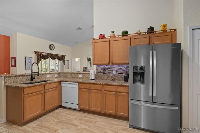 kitchen featuring light stone countertops, sink, white dishwasher, and stainless steel refrigerator with ice dispenser