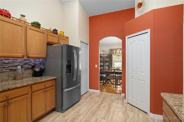 kitchen featuring light stone counters, stainless steel fridge, a towering ceiling, decorative backsplash, and light wood-type flooring