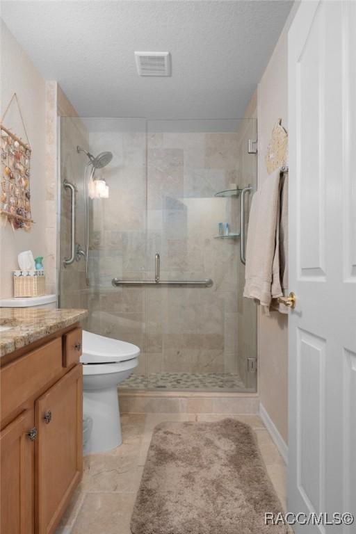 bathroom featuring tile patterned floors, a textured ceiling, toilet, vanity, and a shower with shower door