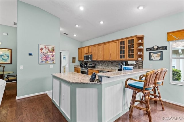 kitchen featuring vaulted ceiling, decorative backsplash, light stone counters, kitchen peninsula, and stainless steel appliances