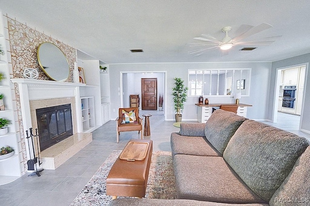 living room with ceiling fan, a fireplace, built in features, and a textured ceiling