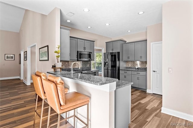 kitchen featuring dark stone counters, stainless steel appliances, gray cabinets, and dark wood-type flooring