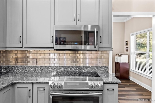 kitchen featuring dark wood-type flooring, dark stone counters, crown molding, gray cabinets, and stainless steel appliances