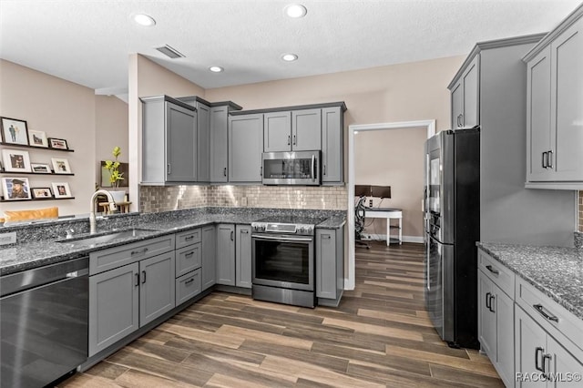 kitchen featuring gray cabinetry, sink, stainless steel appliances, dark wood-type flooring, and dark stone counters