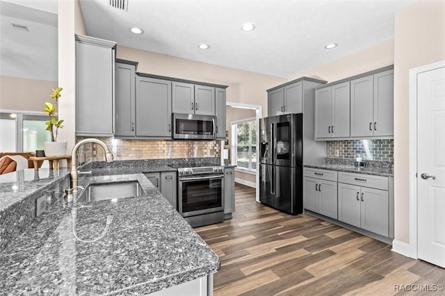 kitchen featuring gray cabinetry, sink, stainless steel appliances, dark hardwood / wood-style floors, and dark stone counters