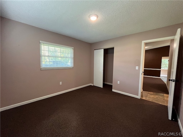 unfurnished bedroom with a closet, dark carpet, and a textured ceiling