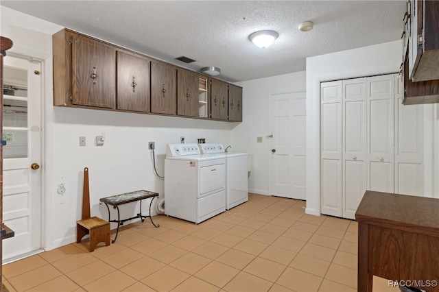 clothes washing area featuring separate washer and dryer, light tile patterned flooring, cabinets, and a textured ceiling