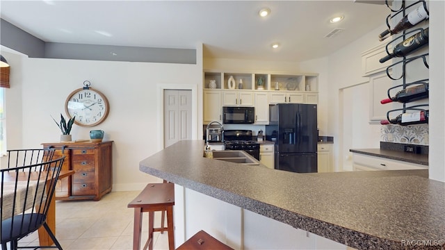 kitchen featuring a breakfast bar area, light tile patterned floors, dark countertops, a sink, and black appliances