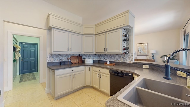 kitchen featuring light tile patterned floors, dishwasher, dark countertops, cream cabinetry, and a sink