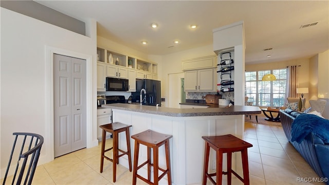 kitchen featuring light tile patterned floors, visible vents, open floor plan, a kitchen breakfast bar, and black appliances