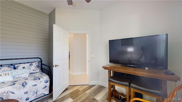 bedroom featuring a ceiling fan, wood walls, baseboards, and wood finished floors